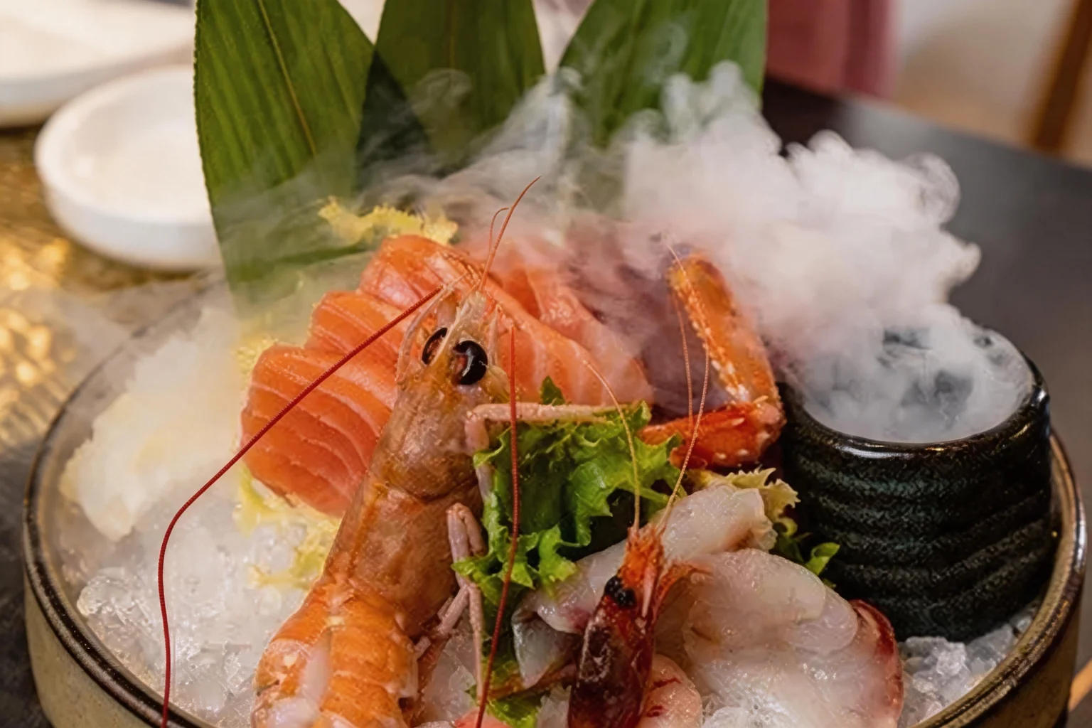 Sashimi di salmone e pesce bianco con gamberi rossi e scampi su ghiaccio, con foglie verdi e fumo di ghiaccio secco.